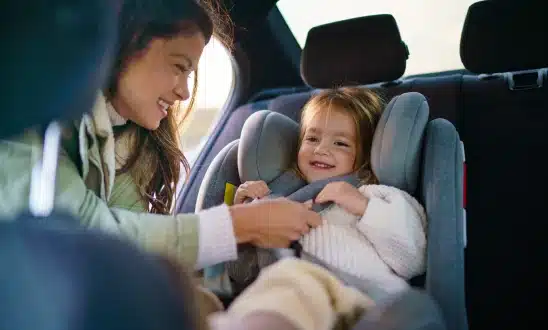 Mother buckling a smiling toddler into a car seat