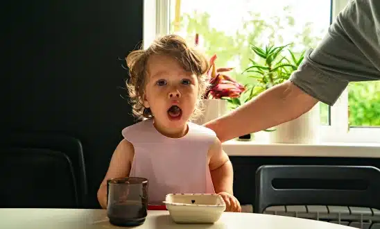 Toddler with a wide-open mouth sitting at a table