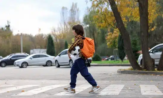 Child with a backpack walking near a crosswalk